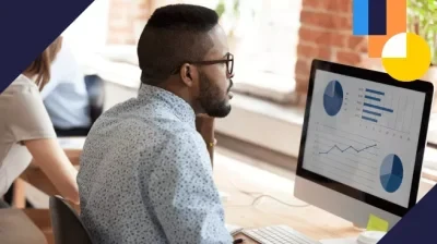 Hombre en una oficina, usando lentes, analiza un panel de gráficas e indicadores en una computadora con una interfaz de datos superpuesta en la pantalla, lo que sugiere análisis de rendimiento y estadísticas.