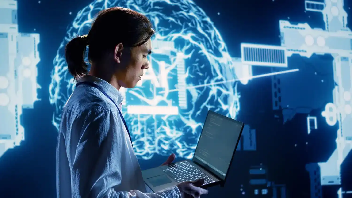 Hombre usando una laptop en un entorno tecnológico con un holograma de cerebro digital al fondo, simbolizando innovación e inteligencia artificial en la era digital.